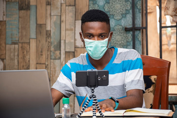young black man working from home wearing a face mask, vlogger working at home, creating content