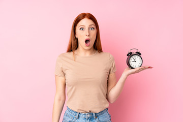 Young redhead woman over isolated pink background holding vintage alarm clock
