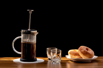 Coffee brewing in a French press pot and two donuts in plate on the wood table and warm morning light, Selective focus.