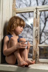 a boy with blond hair sits on a windowsill