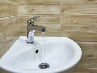 Modern open water tap in the bathroom with flowing water in sink.