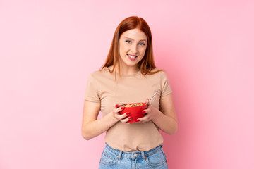 Young redhead woman over isolated pink background holding a bowl of cereals