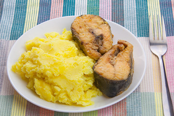 Boiled mashed potatoes on a plate with fried salmon on table
