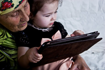 Grandmother and a small child are watching a tablet. A child and grandmother are playing at home on a picture during a coronary outbreak.