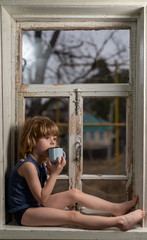 a boy with blond hair sits on a windowsill