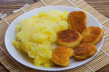 Boiled mashed potatoes on a plate with chicken nuggets on table