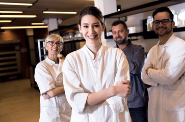 Fototapeta na wymiar Portrait of young female baker at bakery with her colleagues in backgrounds.
