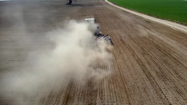 Aerial view tractor cuts furrows in farm field for sowing farm tractor with rotary harrow plow preparing land for sowing.