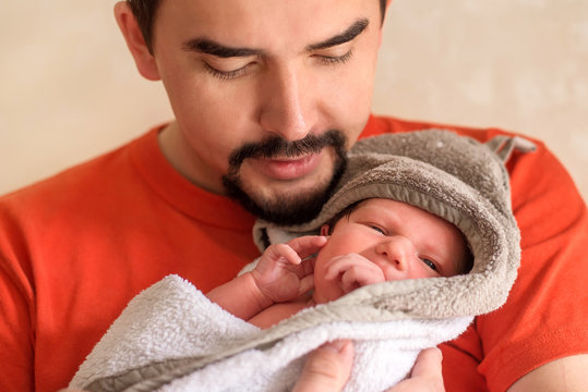 Young father holding in arms little newborn baby daughter after bathing. Portrait of infant child wrapped in towel or blanket in arms of dad. Parenting, responsibility, man on parental leave concept