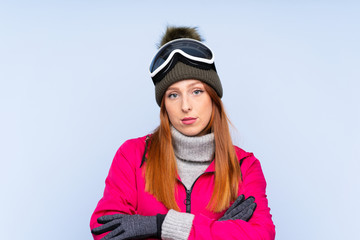 Skier redhead woman with snowboarding glasses over isolated blue wall keeping arms crossed