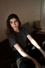 portrait of a girl with brown hair, sitting at home on the bed, look out the window