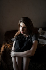 Fototapeta premium portrait of a girl with brown hair, sitting at home on the bed, look out the window