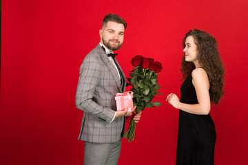 Man with flowers presenting gift to girlfriend in valentine day isolated on red background