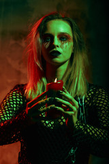 close up portrait of beautiful sexy witch with halloween makeup. red and black face painting. chain in hands