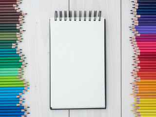 two rows of colored pencils and notebook on wooden background