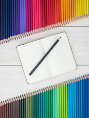 notebook and two rows of colored pencils on wooden background