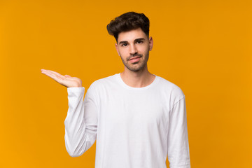 Young man over isolated orange background holding copyspace imaginary on the palm to insert an ad