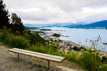Bench on the mountain Aksla at the Alesund cityscape background whit architecture of city in Art Nouveau, Neoclassical and neo-Gothic  style. Sun rays illuminate Atlantic Ocean and islands. Norway.
