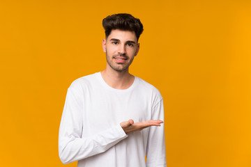 Young man over isolated orange background presenting an idea while looking smiling towards