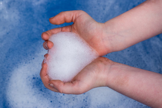 Closeup Of Cupped Hands With Soap Bubbles Shaped Like Heart Over Soapy Water