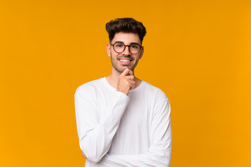 Young man over isolated orange background with glasses and smiling