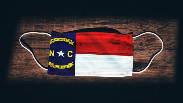 North Carolina Flag. Coronavirus Covid 19 in U.S. State. Medical mask isolate on a black background. Face and mouth masks for protection against airborne infections in USA, America