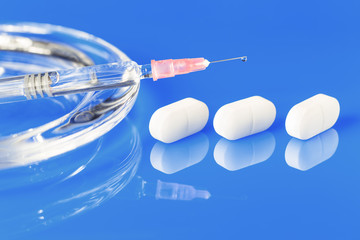 one glass syringe with a drop and white pills on glass plate with copy space close up view....