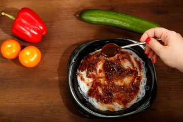A female hand pours ready-made funchose in a black plate with pattaya sauce.
