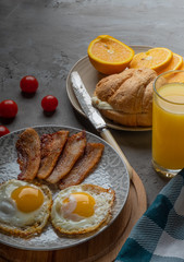 Breakfast of fried eggs with raw yolk, orange juice, orange and croissant.