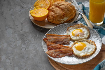 Classic breakfast of fried eggs, orange juice, orange and croissant on a wooden board, brown texture background