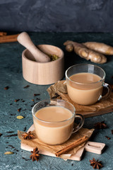 Glass cups of traditional Indian masala chai on dark green texture background. Ingredients of beverage black tea, ginger, cinnamon, cardamom, anise stars
