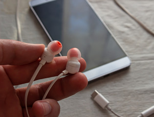 A man is holding a phone earphone in his hands. Headphones in hand on the background of a smartphone. The phone is on the table.