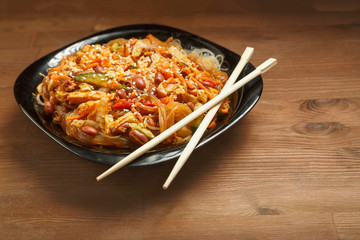 Black plate with funchose and chicken on a wooden table and chopsticks.