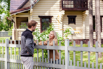 Middle aged man meeting smiling female neighbor in countryside and talking cheerfully to her over fence - Powered by Adobe