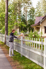 Middle aged man and his female neighbor standing in countryside and talking over wooden fence
