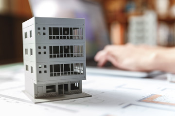 Close up of a house model standing over apartment plans in front of a laptop in a construction...