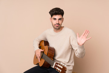 Young man with guitar over isolated background saluting with hand with happy expression