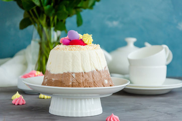 Easter cake. Cottage cheese Easter Paskha Three chocolates with coconut and candy eggs on top on a white plate on a concrete background with flowers. Horizontal orientation. Copy space.