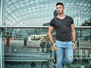 One handsome young man in urban setting in European city, wearing jeans and black t-shirt