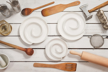 Białe stylowe miseczki leżą na białych drewnianych deskach. Wokoło leżą stare stylowe naczynia kuchenne tworzą tło.