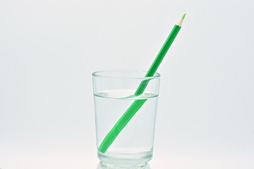 Lápiz de color verde dentro de un vaso de agua, refracción de la luz