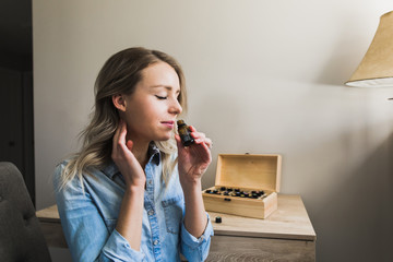 Young woman applying essential oils to her neck and smelling open bottle - obrazy, fototapety, plakaty