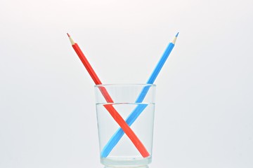 Lápices de color azul y rojo, dentro de un vaso lleno  de agua, explicación de la  refracción de...