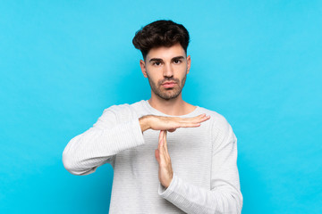 Young man over isolated blue background making time out gesture
