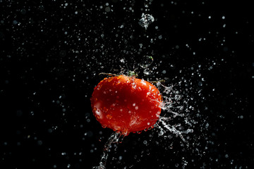 Fresh red tomato in a splash of water on a black background