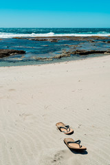 Flip flops on sandy beach at the seaside. Sea waves in the background. Empty beach. Vacation concept