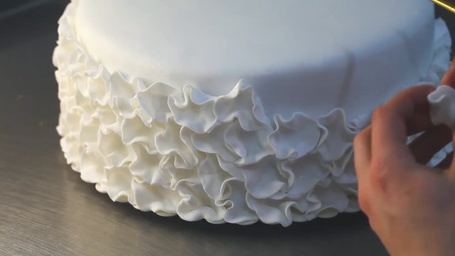 A confectioner decorates a white wedding cake with sugar mastic flowers