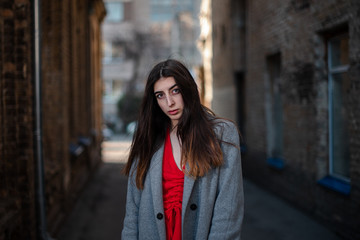 Fototapeta premium Girl in a red blouse and a gray cardigan on the background of the old brick wall