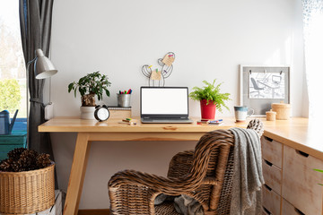 Office desk with laptop in cozy interior in scandinavian style with white wall with copy space, Home office during coronavirus. Empty screen with mock up. Workspace and stylish design.