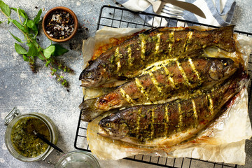 Baked salmon fish with pesto sauce and culinary spices on a gray stone countertop. Top view flat lay background.